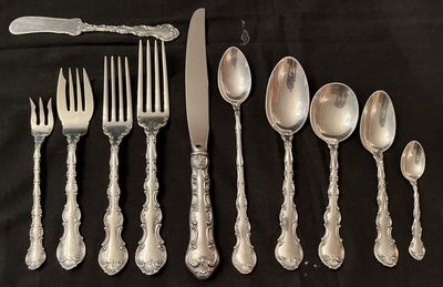 A sterling silver place setting laid out on black velvet: forks, a knife, and spoons in a scrolled pattern