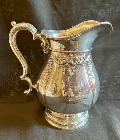 A sterling silver water pitcher with a scrolled handle and chased floral band