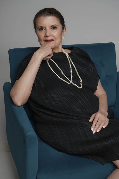 Suzanne Staley seated in a teal armchair, wearing a black dress and a long strand of pearls