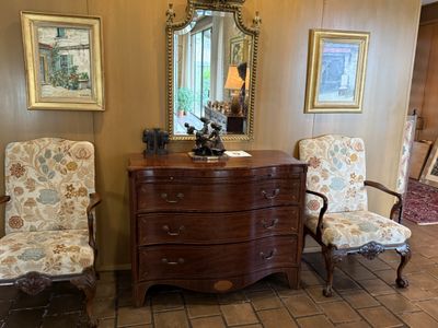 A serpentine-front mahogany chest beneath a gilt mirror, flanked by a pair of floral upholstered armchairs