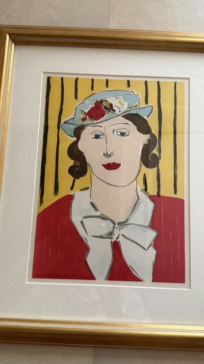 A framed portrait of a woman in a flowered hat and red jacket