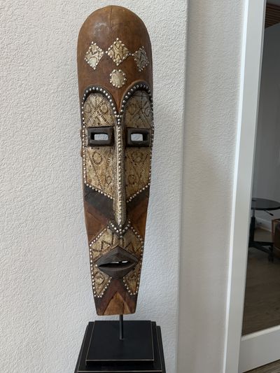 A carved wooden mask inlaid with shell and beadwork, mounted on a stand