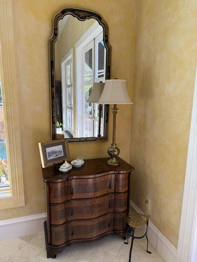 A serpentine-front chest below an arched mirror, with a lamp and framed print